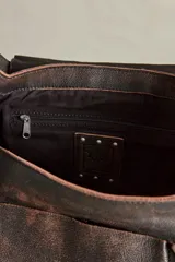 Cartera hobo de cuero marrón con efecto desgastado, solapa frontal con ojales metálicos y tira con hebilla. Cuenta con bolsillos laterales con solapa y herrajes metálicos plateados.