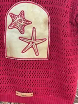 Saco de punto abierto color rojo con un parche grande de cuero dorado aplicado en el frente, que cuenta con bordados de estrellas de mar.