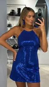 Vestido corto de fiesta confeccionado en tela con lentejuelas azules. Presenta un diseño ajustado al cuerpo con escote halter y espalda descubierta.