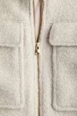 Campera corta de tejido bouclé en color beige, con cuello clásico, cierre frontal con cremallera y bolsillos frontales con solapa. Presenta un diseño forrado y estructurado.