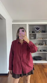 Camisa de manga larga con diseño de rayas verticales en color bordó. Presenta cuello clásico, cierre frontal con botones y un bolsillo en el pecho. Su corte es holgado y cómodo.