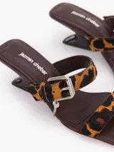 Sandalia de taco bajo con estampa animal print de leopardo, tiras finas de cuero, hebilla metálica y dijes colgantes.