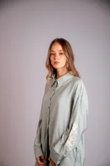 Camisa beige de corte amplio, con cuello clásico, cierre frontal con botones, mangas largas con puños abotonados y bordado floral en las mangas.