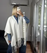 Poncho de tejido suave color blanco, con diseño abierto y flecos en el ruedo inferior.