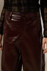 Pantalon de eco-cuero con diseño barrel, de tiro alto y corte holgado. Cuenta con bolsillos laterales y cierre frontal con botón.