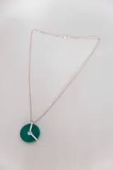 Collar plateado con dije circular de color verde esmeralda y apliques plateados.