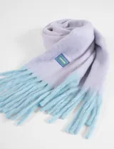 Bufanda de tejido suave en color lila con flecos en tono celeste y detalle de etiqueta con logo en la parte inferior.