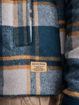 Chaqueta de lana con cierre frontal completo, diseño a cuadros en tonos azul marino y verde, cuello camisero y bolsillos laterales.