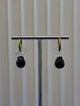 Aros de argolla dorada con dije colgante compuesto por una pieza de vidrio transparente en forma de espiral y una pieza de vidrio negro en forma de gota.