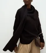 Suéter de punto color negro con fit holgado, mangas largas, cuello alto y bufanda integrada con caída frontal. Presenta puños y ruedo acanalados.