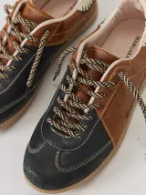 Championes de cuero con diseño tricolor en tonos negro, marrón y crema. Presentan cordones trenzados, costuras a la vista y detalle de pespuntes en el talón.