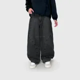 Pantalón de jean estilo ultra baggy, color negro con efecto lavado. Presenta un diseño de corte amplio con costuras curvas decorativas en el frente y bolsillos laterales.