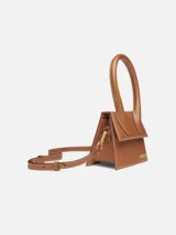 Bolso mini de cuero color marrón, con asa corta reforzada y correa larga extraíble. Cierre magnético, bolsillo interior y herrajes metálicos dorados.