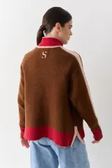 Campera de tejido de punto con cierre frontal, cuello alto y diseño color block en tonos marrón, rosa y rojo. Presenta detalles de trenzas en las mangas y puños y ruedo acanalados.