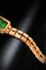 Reloj de pulsera con caja cuadrada de madera de olivo y esfera verde con marcadores minimalistas y agujas doradas. La malla es de madera de olivo con eslabones centrales metálicos en tono dorado.
