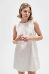 Vestido corto de jean blanco con tirantes anchos, cuello redondo, corte holgado y bolsillos laterales.