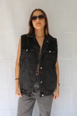 Chaleco negro de denim con cuello clásico, cierre frontal con botones metálicos, bolsillos con solapa en el pecho y terminaciones desflecadas en sisas y ruedo.