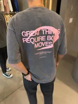 Remera de algodón pesado con efecto lavado, corte oversize y estampa gráfica en color rosa en la espalda con la frase Great Things Require Bold Moves.