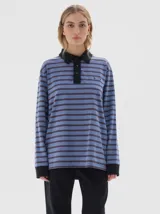 Chomba de manga larga con diseño a rayas horizontales en tonos azul y gris. Presenta cuello polo y cartera de botones en color negro, con puños negros y bordado pequeño en el pecho.
