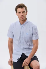 Camisa de manga corta a rayas celestes y blancas, con cuello abotonado, bolsillo frontal con logo bordado y cierre frontal de botones.