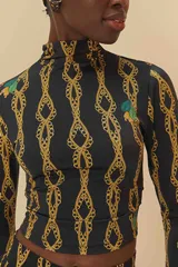 Top negro con estampado de cadenas doradas, cuello alto y mangas largas.