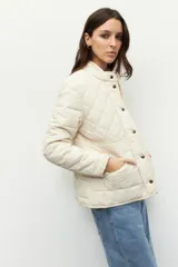 Campera capitoneada color beige, de cuello alto, con bolsillos de solapa y botones metálicos.