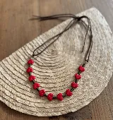 Collar corto con cuentas rojas en forma de flor y pequeñas cuentas metálicas color bronce, engarzadas en un cordón de cuero marrón con cierre ajustable.
