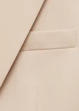 Chaqueta tipo blazer de corte entallado en color beige, con cuello de solapas con muesca, hombros estructurados, cierre frontal de un botón y bolsillos de ribete delanteros.