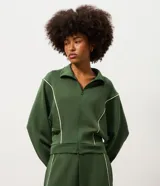 Campera deportiva de microfibra color verde oscuro, con cuello alto, manga larga y cierre frontal. Presenta recortes estructurados con vivos contrastantes claros, barra ajustada y puños alargados.