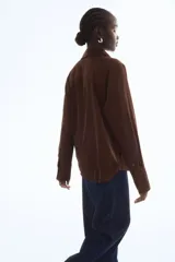 Blusa de manga larga color marrón oscuro, con cuello clásico y escote en V profundo, cierre frontal de botones y puños anchos.