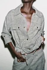 Chaqueta jaspeada color beige, con cuello solapa, manga tres cuartos con trabilla y botón, bolsillos delanteros de plastrón con solapa, bajo ajustable con cordones interiores y cierre frontal con botones a presión.