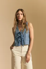 Chaleco corto sin mangas, color azul con estampado geométrico en blanco. Presenta escote en V pronunciado y lazos ajustables en el centro frontal.