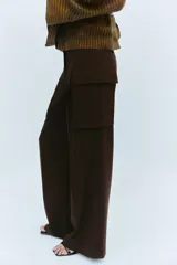 Pantalón cargo de tiro medio en color marrón oscuro, con corte recto y amplio. Presenta bolsillos laterales tipo cargo con solapa y detalle de pliegues frontales. Cierre frontal con cremallera y botón.