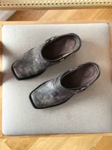 Zueco de cuero con efecto desgastado en tono visón, con diseño de punta cuadrada, suela gruesa negra y detalle de correa con tachas metálicas y argolla lateral.