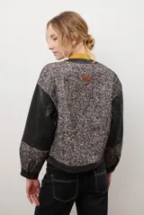Chaqueta bomber color bordó con mangas de cuero sintético marrón y cuerpo de tweed con patrón de espiga. Cierre frontal con botones a presión y cuello redondo.