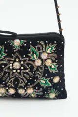 Cartera de mano o bandolera pequeña de terciopelo negro con bordado floral multicolor y apliques de lentejuelas y cuentas brillantes. Correa delgada negra con tachas doradas.