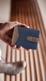 Billetera de formato mediano, combinando símil cuero marrón desgastado y tela canvas azul marino. Posee una presilla de cierre exterior, visor interior, doble compartimento para billetes y tarjeteros.