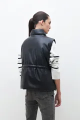 Chaleco negro de cuero sintético con cuello alto, cierre frontal con cremallera y bolsillos laterales con solapa.