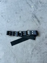 Cinturón negro de cuero con argollas plateadas.