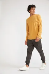 Remera de manga larga color mostaza, con cuello redondo y estampado frontal con las siglas MST en contorno verde.