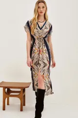 Vestido midi estampado con cuello en V y mangas cortas. Presenta un diseño con cordón ajustable a la cintura y abertura frontal en la falda. El estampado es de estilo étnico o tribal en tonos beige, negro, amarillo y rojo.