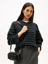 Cartera estilo camera bag negra, estructurada y compacta, con textura integral de monograma TH en relieve y placa metálica dorada con el logo TH en el frente. Posee cierre superior y correa ajustable para llevar al hombro o cruzada.