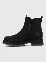 Bota corta tipo Chelsea de cuero negro, con elásticos laterales y suela track gruesa de goma translúcida gris.