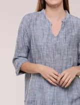 Blusa de silueta relajada con textura tramada, color azul con rayas verticales en tonos rosados, celestes y amarillos. Cuenta con cuello mao abierto en V y mangas tres cuartos amplias con pequeña abertura lateral en el puño.