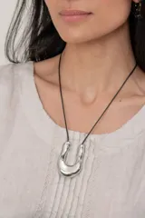 Collar minimalista con cordón negro y dije colgante de metal plateado con diseño orgánico y acabado brillante.