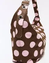 Cartera tipo hobo de color marrón con estampado de lunares rosados, asa ajustable con hebilla metálica y ojalillos.