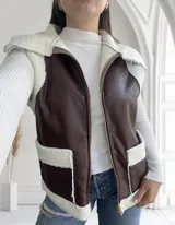 Chaleco marrón de ecocuero con interior de corderito blanco, cierre frontal con cremallera y bolsillos laterales.