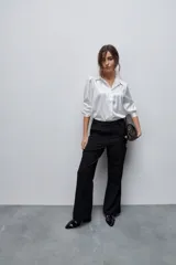 Camisa blanca de calce relajado con acabado satinado y brillo sutil, cuello clásico, cierre frontal con botones y mangas largas con puños.