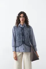 Chaleco de punto con efecto jaspeado en color azul, con diseño sin mangas, escote redondeado y cierre frontal mediante lazos ajustables.