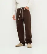 Pantalón masculino de corte baggy, confeccionado en sarga de algodón. Presenta un diseño holgado con costuras en contraste, cierre tradicional y cordón ajustable en la cintura.